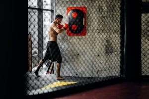 Sportsman with a naked torso and in the red boxing gloves hits equipment for boxing on a concrete